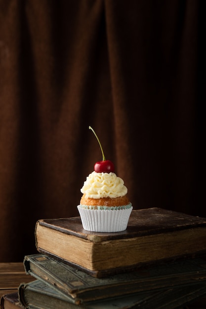 Vertical shot of a delicious cupcake with cream and cherry on top on books