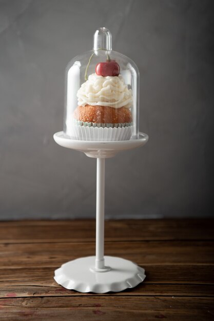 Vertical shot of a delicious cupcake with cream and cherry on top on a dessert stand