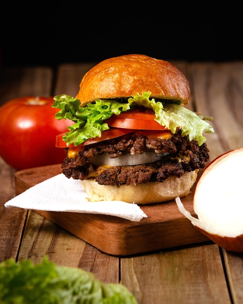 Vertical shot of a delicious hamburger on a wooden plate with a black background