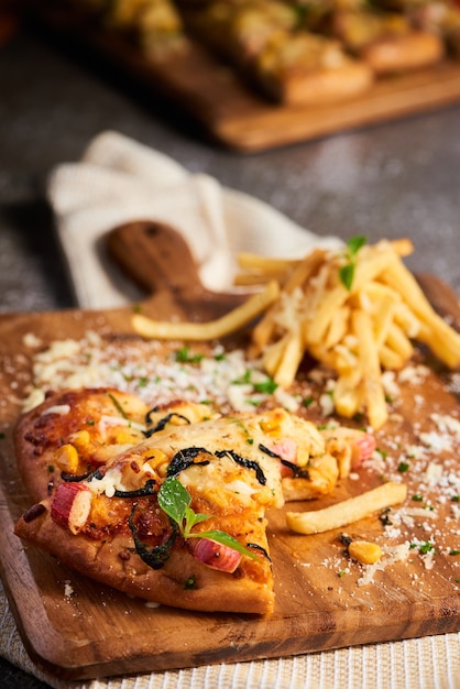 Vertical shot of delicious pizza served with fries on a wooden board