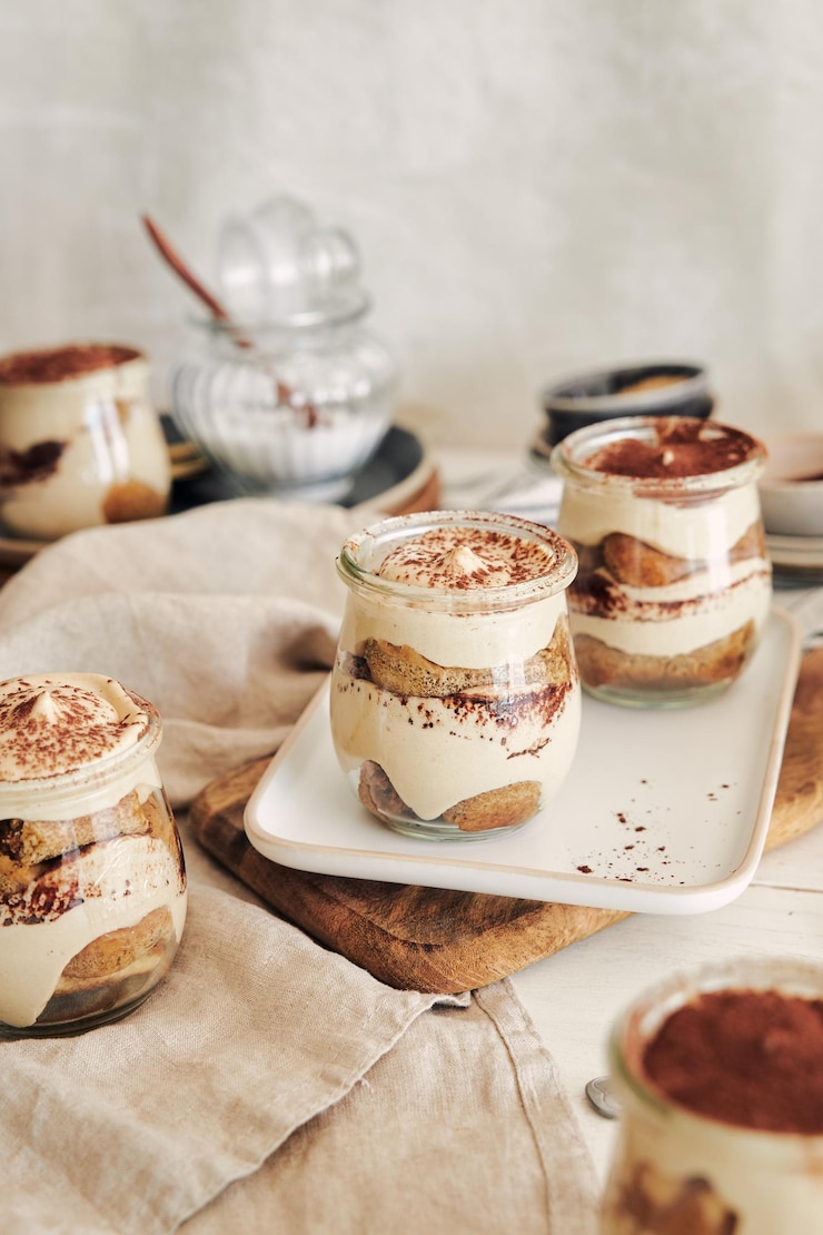 Бесплатный Фотография вертикальный снимок вкусного тирамису в стаканчиках с порошком на белом столе