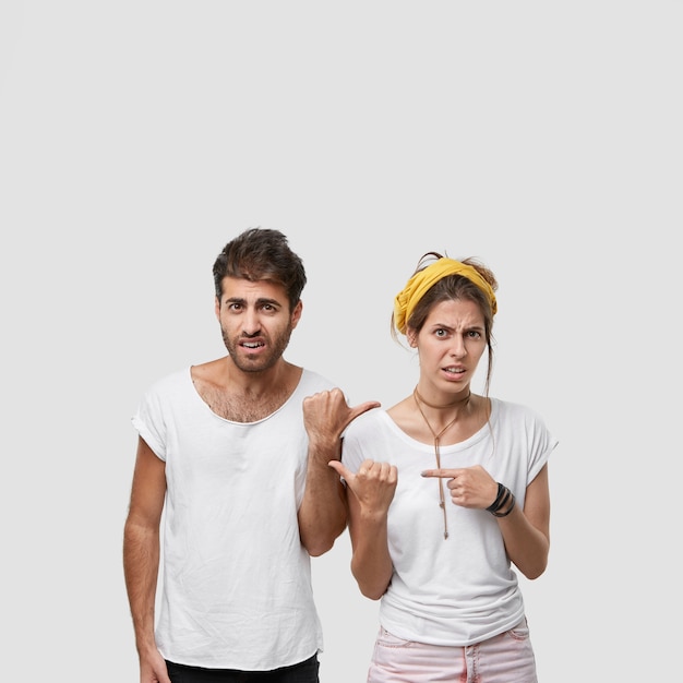 Free photo vertical shot of dissatisfied european feminine and masculine adults point at each other, express negative emotions, feel depressed, stand closely, dont want to do housework