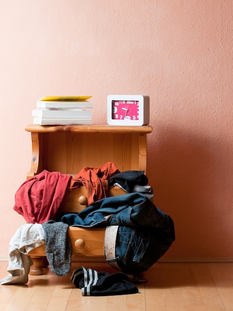 Free photo vertical shot of a drawer with several clothes on it together with books and a clock