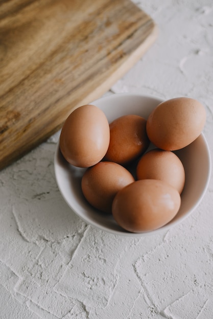 Vertical shot of eggs in a bowl next to a chopping board on the table