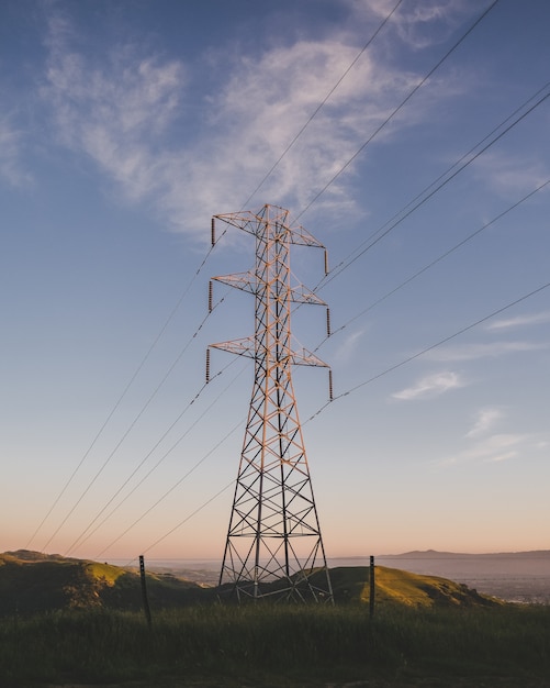 Vertical shot of an electric tower on a grassy field under a blue sky