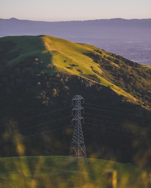 Vertical shot of an electric tower on a grassy mountain