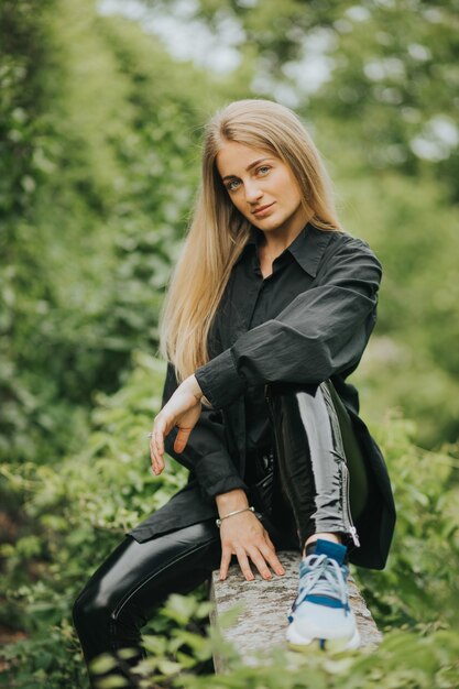 Vertical shot of a fashionable caucasian blonde female posing surrounded by greenery