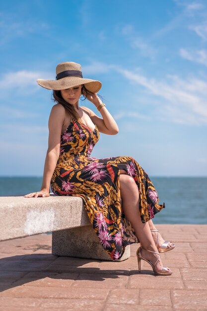Вертикальный снимок женщины в цветочном платье и шляпе на берегу океана в Сан-Себастьяне, Испания.