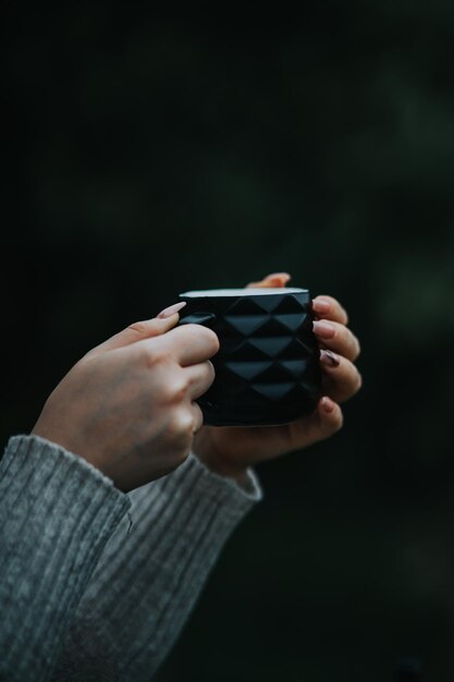 Vertical shot of female hands in a cozy sweater holding a black coffee cup
