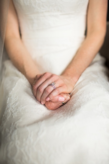 Colpo verticale di una donna in un lungo abito bianco seduto con le mani sulle ginocchia