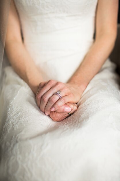 Vertical shot of a female in a long white dress sitting with her hands on her knees