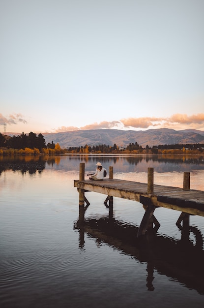 Free photo vertical shot of a female sitting on the pier playing the guitar in cromwell, new zealand