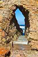 Free photo vertical shot of a female standing in front of a cave leading to the ocean