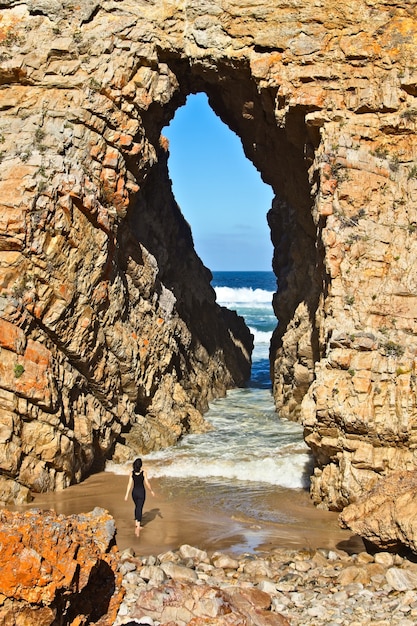 海につながる洞窟の前に立っている女性の垂直ショット