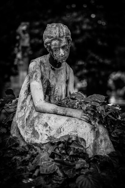 Vertical shot of a female statue  surrounded by leaves in black and white