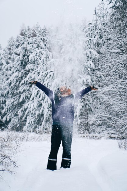 冬の森で空中に雪を投げる女性の垂直ショット