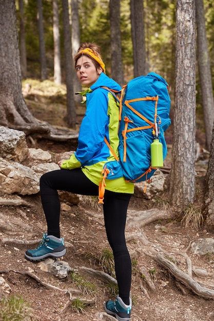 Вертикальный снимок женщины-туристки, идущей в горном лесу, оглядываясь назад, преодолевая большое расстояние в гору