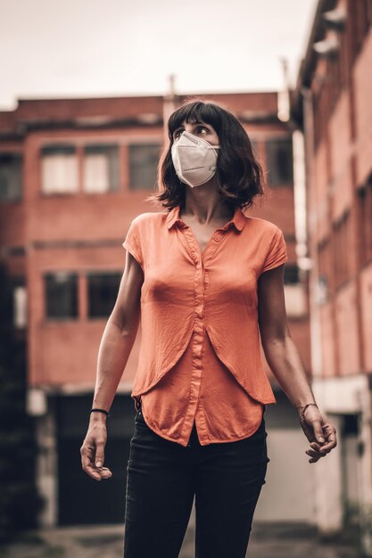Ripresa verticale di una donna che indossa una maschera facciale e cammina in un quartiere - covid-19