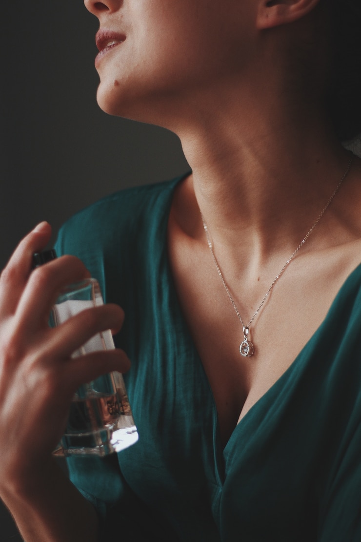 Free Photo vertical shot of a female wearing a necklace with a diamond pendant spraying perfume on her