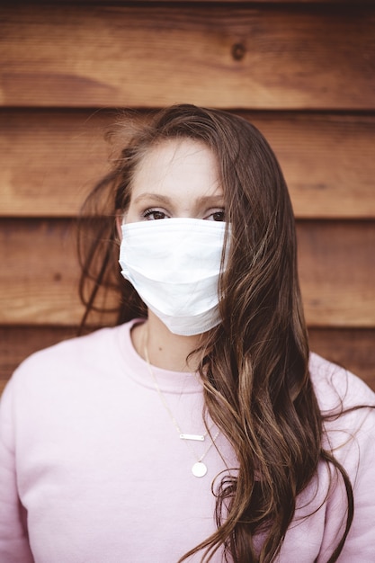 Free photo vertical shot of a female wearing a sanitary face mask in front of a wooden wall