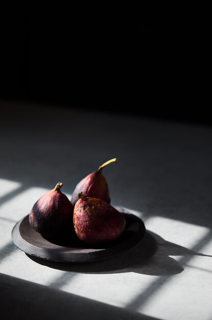 Vertical shot of figs in a wooden plate with sun rays falling on them with a blurred