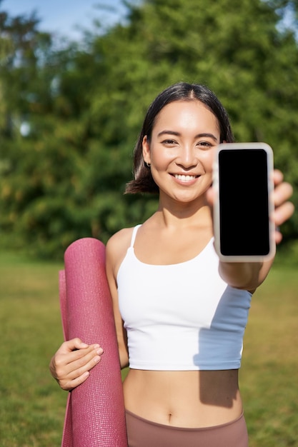 Free photo vertical shot of fit and healthy young asian woman shows smartphone screen with her workout stats