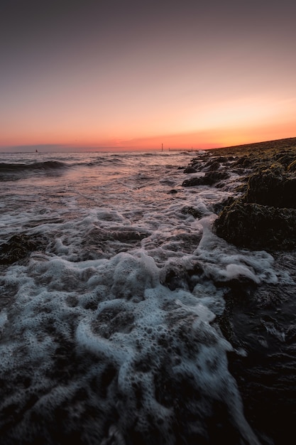 素晴らしい夕日と海岸に来る海の泡立つ波の垂直ショット