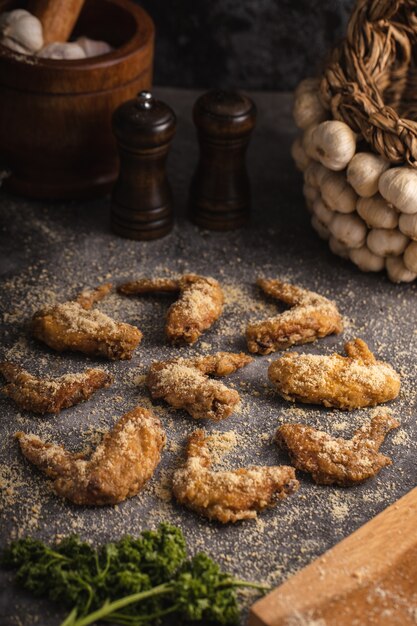 Vertical shot of fried chicken wings and some garlic and spices on a grey surface