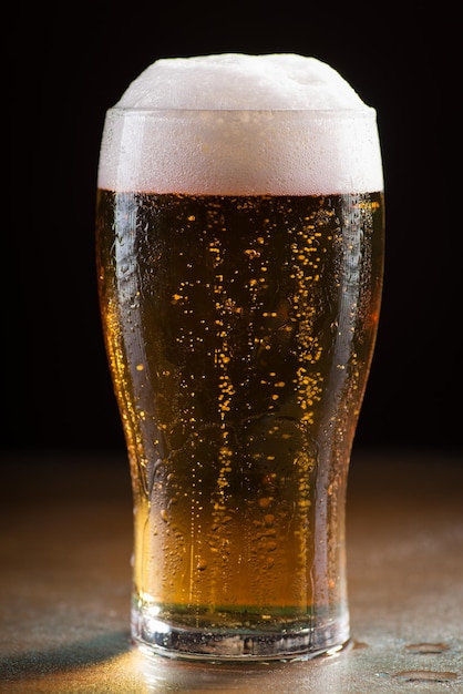 Vertical shot of a glass of cold refreshing beer with foam on a wooden table