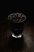 Foto gratuita il colpo verticale di una tazza di vetro ha riempito di chicchi di caffè su una superficie di legno con una priorità bassa nera