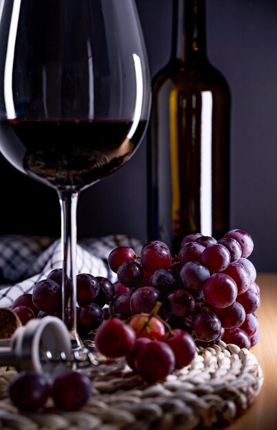 Вертикальный снимок бокала красного вина и винограда на столе