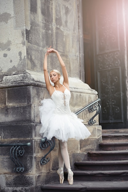 Ripresa verticale di una splendida ballerina che balla sensualmente all'aperto in città posando elegantemente sulla scalinata di un vecchio castello.