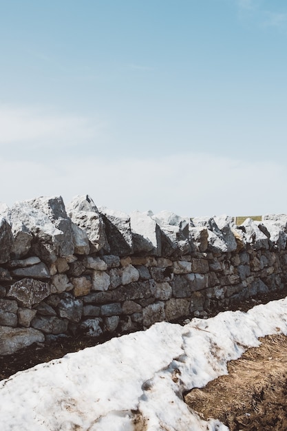 Foto gratuita colpo verticale di un muro di pietra grigio sotto un cielo blu chiaro