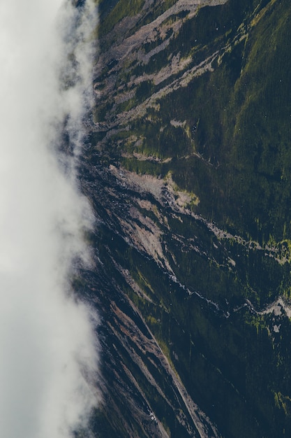 Free photo vertical shot of green mountains covered with white clouds