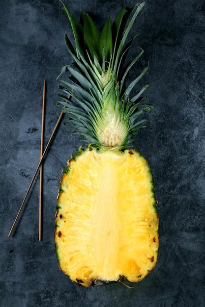 Vertical shot of half of a fresh pineapple and two sticks on the side