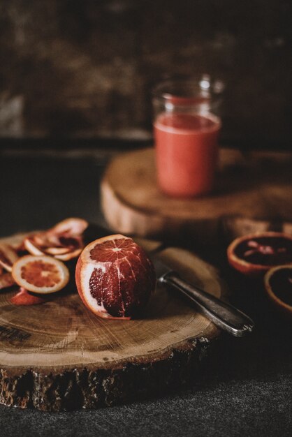Vertical shot of a half peeled blood orange near a knife on a round wooden slab