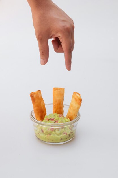 Vertical shot of a hand over a glass jar with cheese tequenos and guacamole sauce