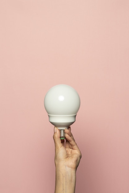 Free photo vertical shot of a hand holding a light bulb isolated on a pink wall