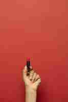 Free photo vertical shot of a hand holding a lipstick isolated on a red wall