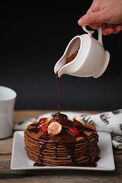 Vertical shot of hand pouring chocolate into pancakes