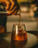 Free photo vertical shot of a hand pouring juice into a glass with ice cubes