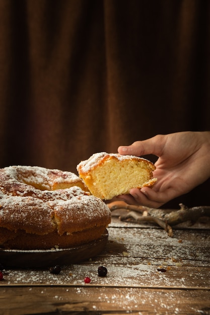 Vertical shot of a hand taking a piece of a delicious sponge cake with powdered sugar