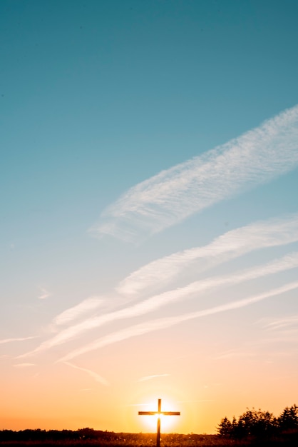 A vertical shot of a handmade wooden cross in the filed with the sun shining behind it