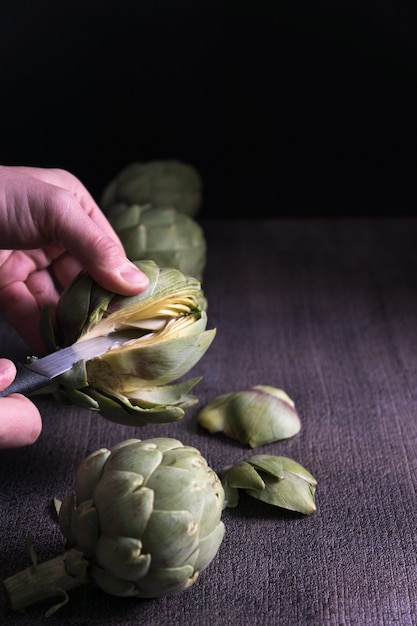 Vertical shot of hands cutting  globe artichokes on a dark surface