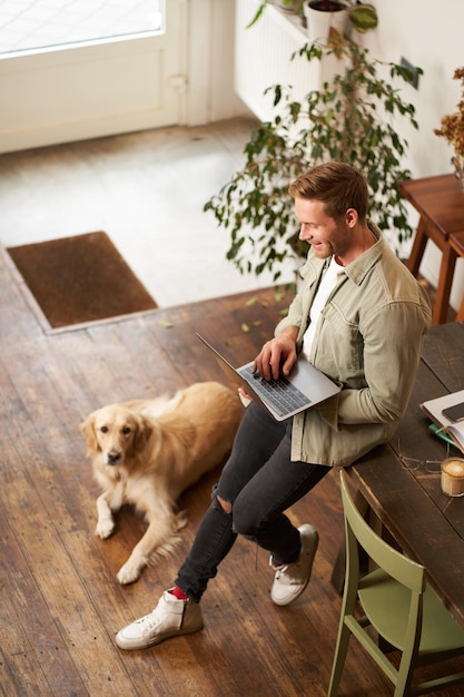 Free photo vertical shot of handsome businessman young man with laptop leans on table sitting at coworking