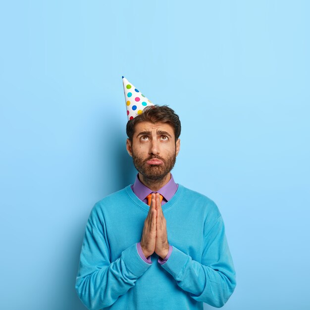 Vertical shot of handsome guy with birthday hat posing in blue sweater