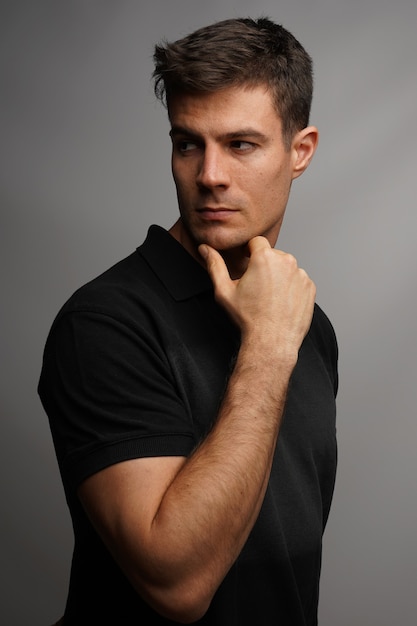 Free photo vertical shot of a handsome man holding his chin with an arm against a gray wall