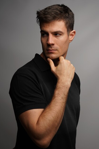 Vertical shot of a handsome man holding his chin with an arm against a gray wall