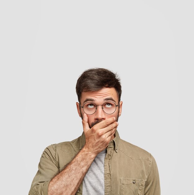 Vertical shot of handsome man with dark hair, keeps hand over mouth