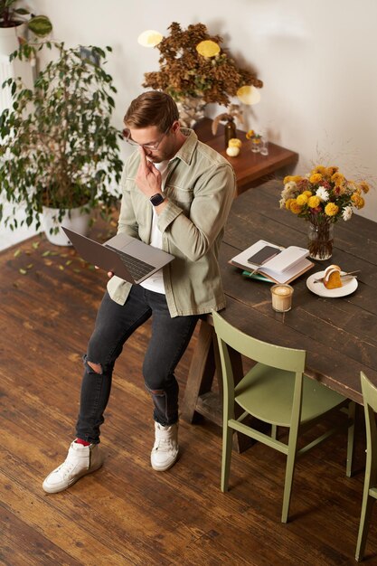 Вертикальный снимок красивого стильного бизнесмена, стоящего возле стола с ноутбуком, думающего о работе